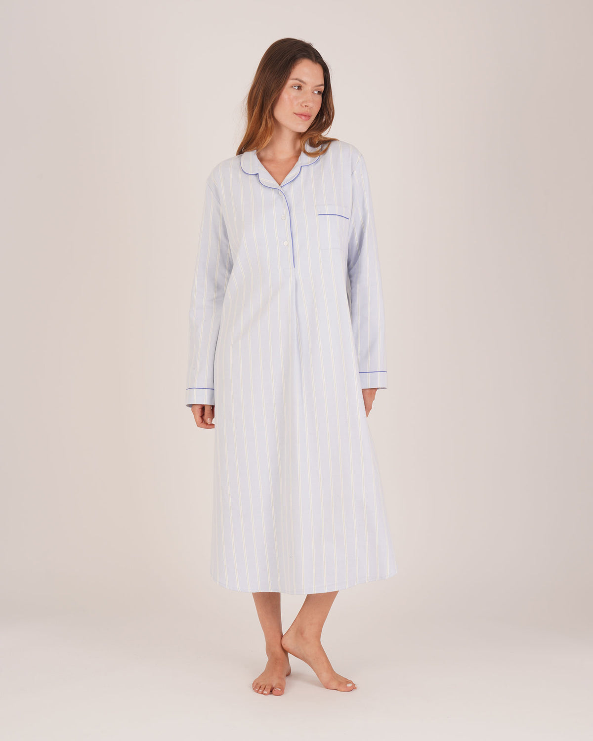 Bonsoir of London Women’s Isla Blue White Stripe Brushed Cotton Nightshirt, featuring a blue and white striped design, button placket, shirt-tail hem, piping detail, cuffs and breast pocket, full body shot on a model.