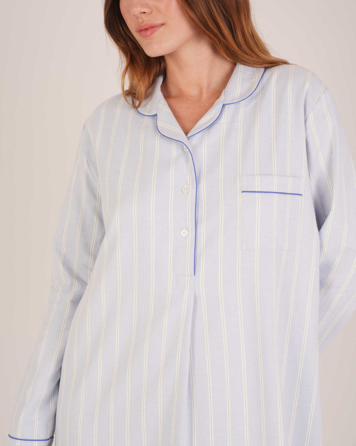 Bonsoir of London Women’s Isla Blue White Stripe Brushed Cotton Nightshirt, featuring a blue and white striped design, button placket, shirt-tail hem, piping detail, cuffs and breast pocket, close up shot on a model.