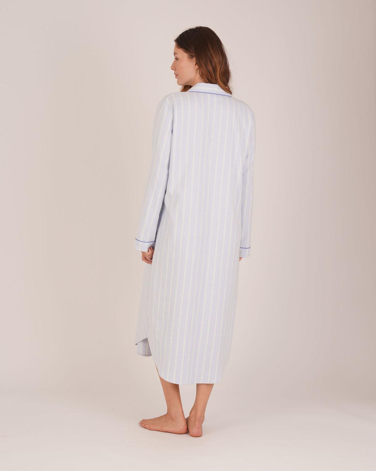 Bonsoir of London Women’s Isla Blue White Stripe Brushed Cotton Nightshirt, featuring a blue and white striped design, button placket, shirt-tail hem, piping detail, cuffs and breast pocket, full body shot on a model from the back.