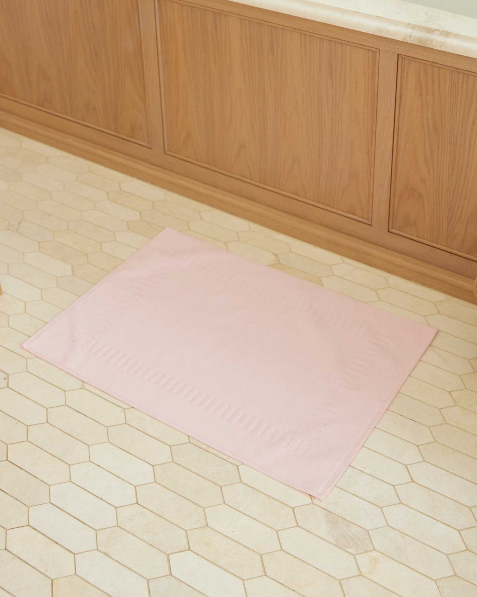 Bonsoir of London 100% Cotton Bath Mat in pink, lifestyle shot on a beige tile floor.
