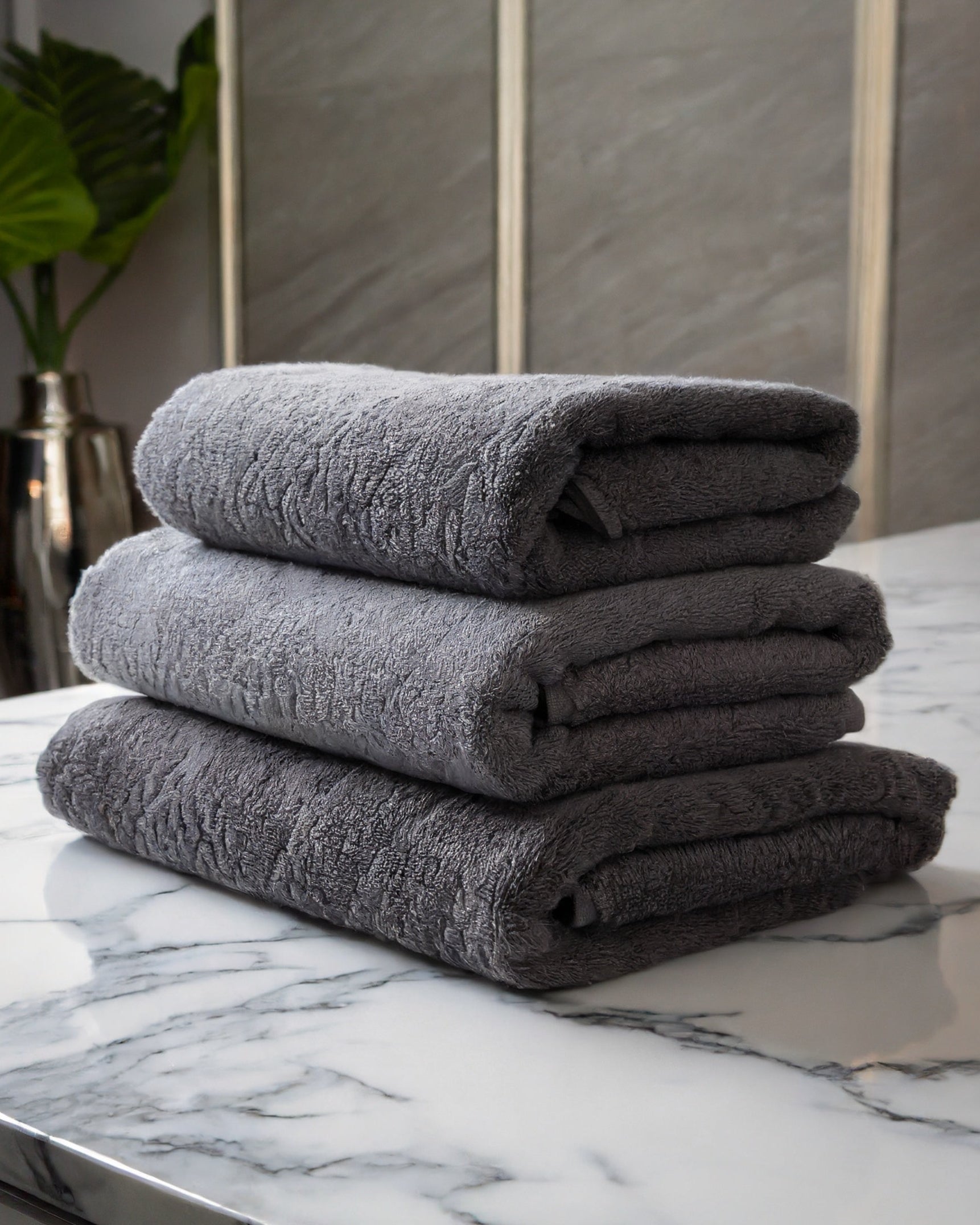 Bonsoir of London stack of grey cotton bath towels on a marble surface.