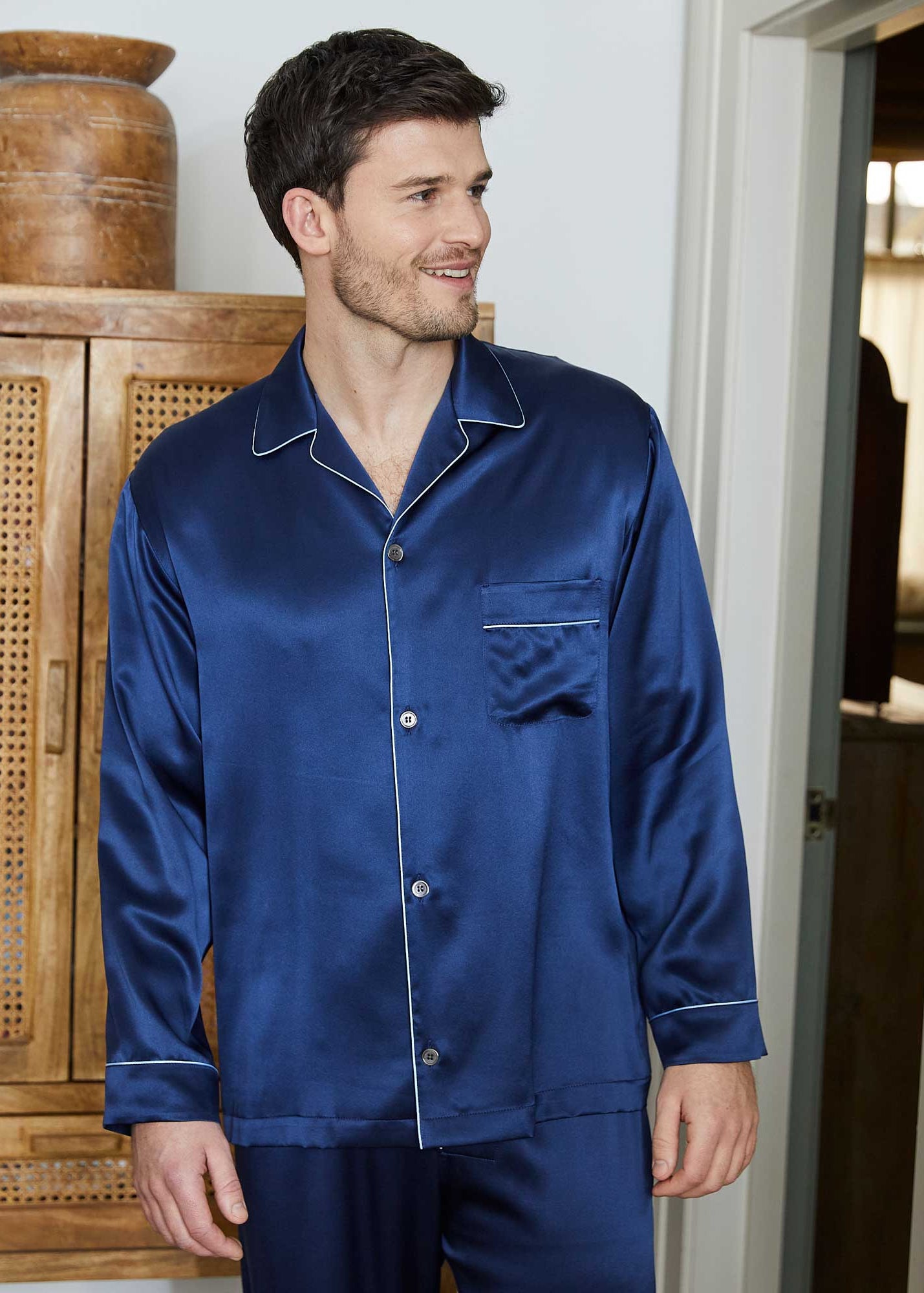Man wearing a blue satin pajama set standing in a room with wooden furniture.