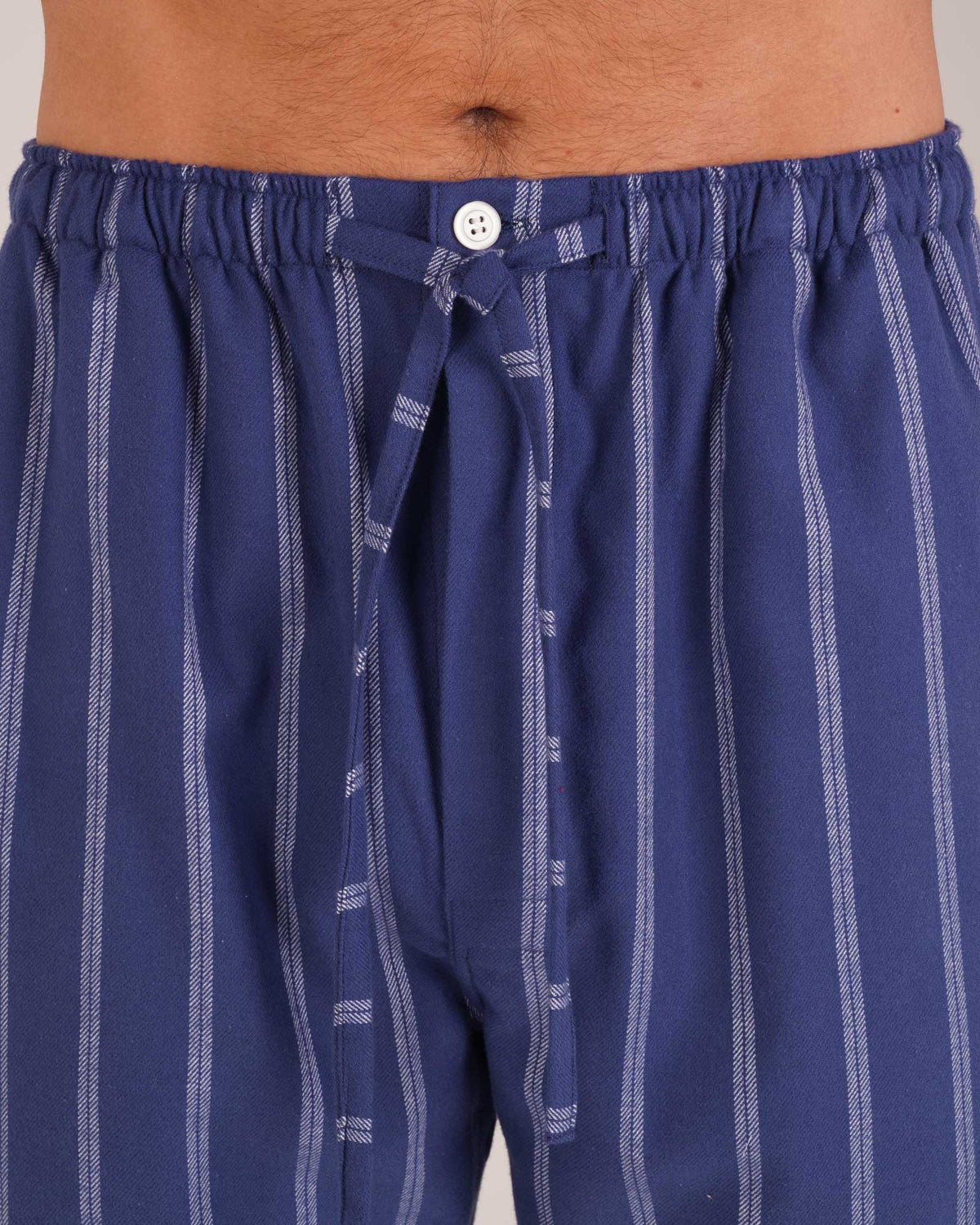 Bonsoir of London Men’s Alexander Navy White Stripe Brushed Cotton Pyjama Trousers, featuring a navy and white striped design, 100% brushed cotton, fully elasticated waist, concealed button fly, self-fabric drawstring tie and pockets, close up shot on a model.