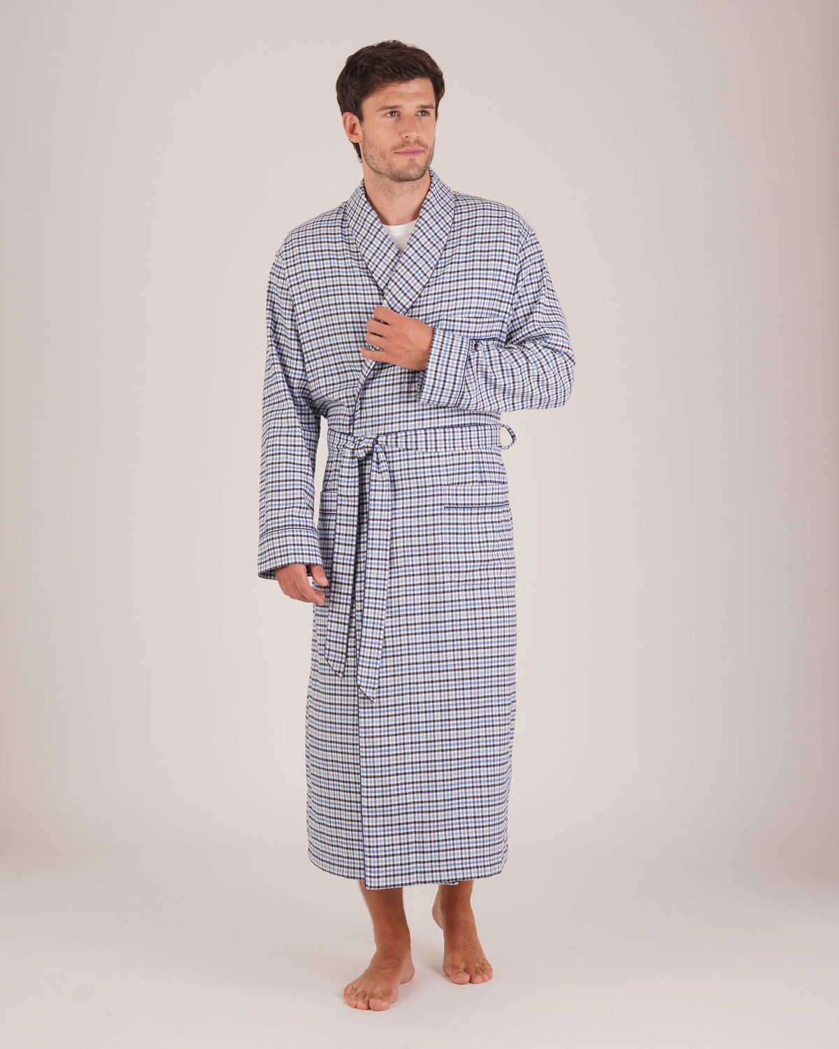 Bonsoir of London Men’s Arthur Blue Check Brushed Cotton Dressing Gown, featuring a soft blue, white and navy check design, shawl collar, wide tie belt, patch pockets, full body shot on a model.