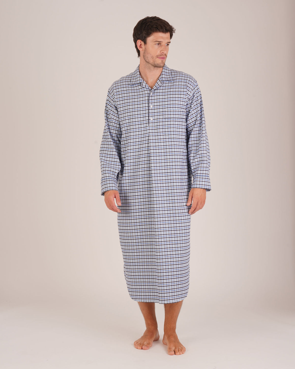 Bonsoir of London Men’s Arthur Blue Check Brushed Cotton Nightshirt, featuring a blue, white and navy check design, four-button placket, shirt-tail hem and generously cut fit, full body shot on a model.