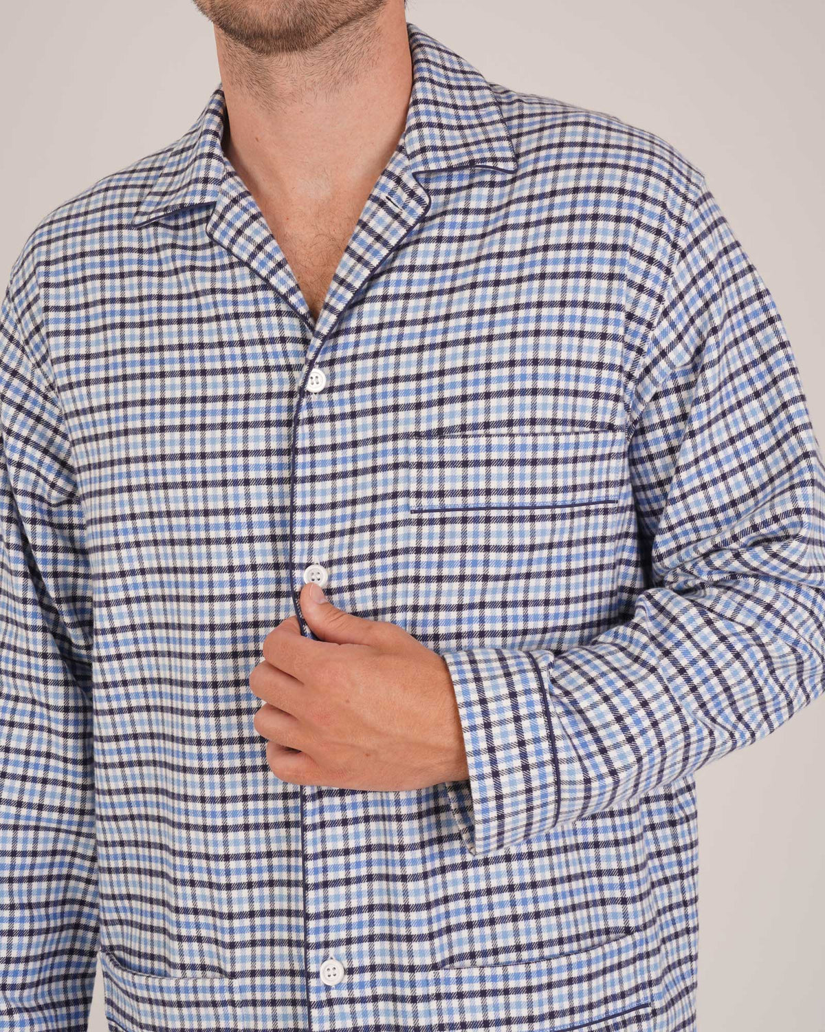 Bonsoir of London Men’s Arthur Blue Check Brushed Cotton Pyjamas, featuring a blue, pale blue, white and navy check design, three jacket pockets, elasticated-waist trousers, button fastening and concealed button fly, close up shot on a model.