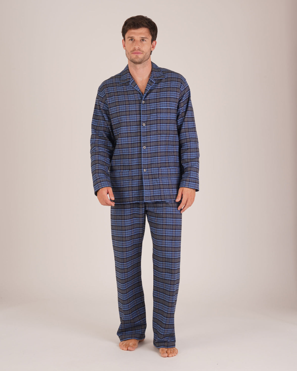 Bonsoir of London Men’s Theodore Blue Plaid Brushed Cotton Pyjamas, featuring a blue and navy plaid design with subtle gold detailing, three jacket pockets, elasticated-waist trousers, button fastening and concealed button fly, full body shot on a model.