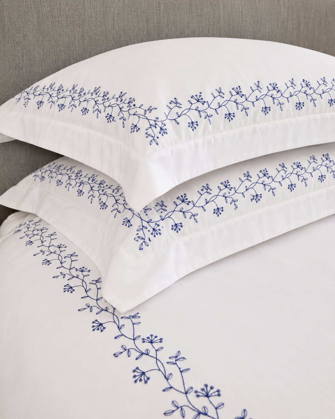 Bonsoir of London white pillows with navy floral embroidery against a grey headboard.