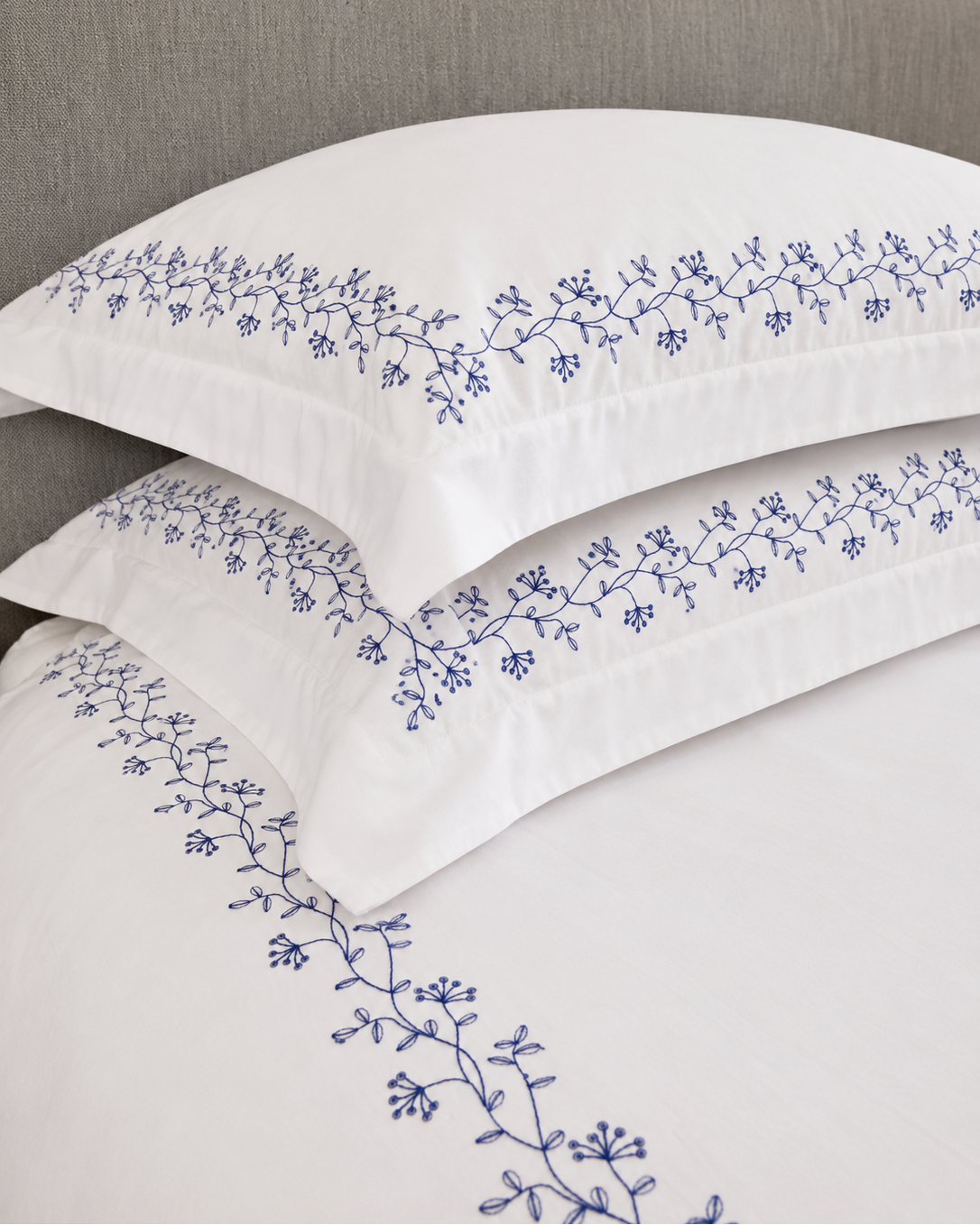 Bonsoir of London white pillows with navy floral embroidery against a grey headboard.