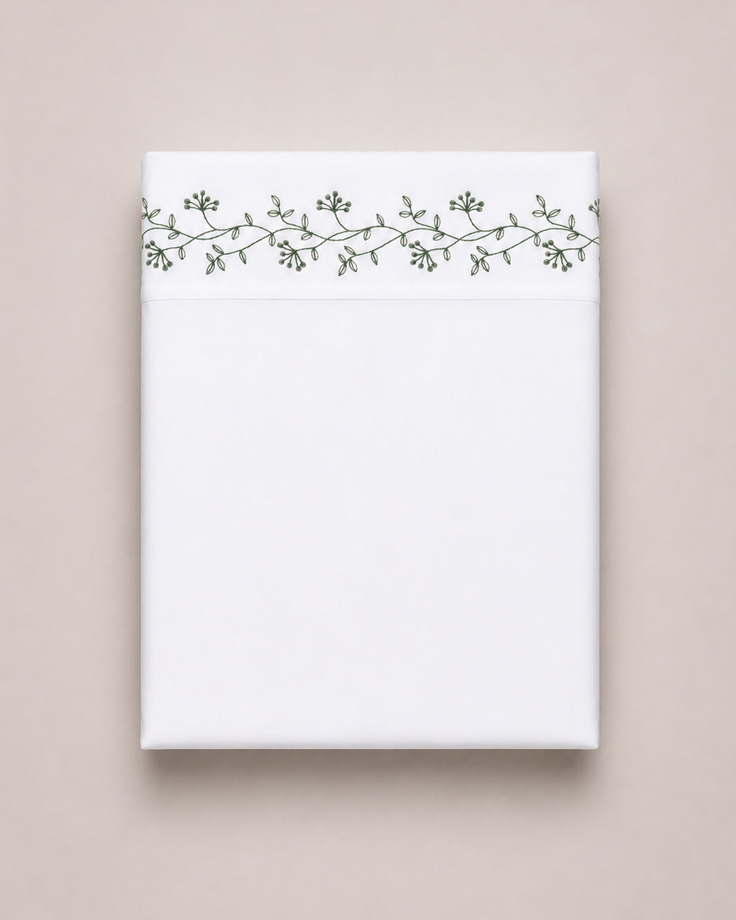 Bonsoir of London cotton white flat sheet with green floral embroidery, folded on a beige studio background.