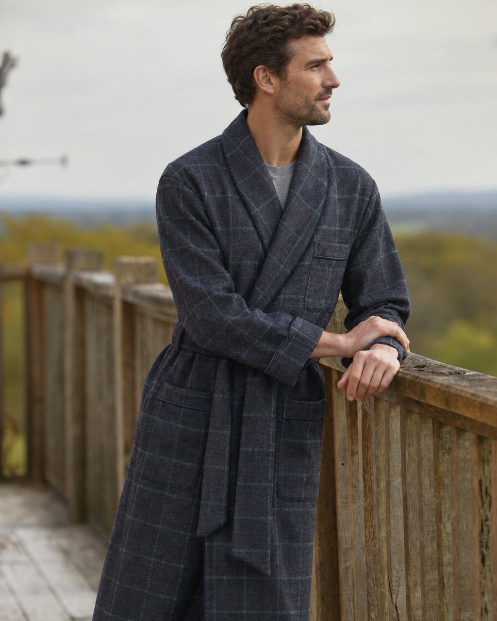 Bonsoir of London Men’s Thomas Check Silk-Lined Wool Robe, featuring a charcoal grey wool fabric with subtle teal green check design, silk lining, shawl collar, three pockets, turn-back cuffs and wide tie belt, full body shot on a model.