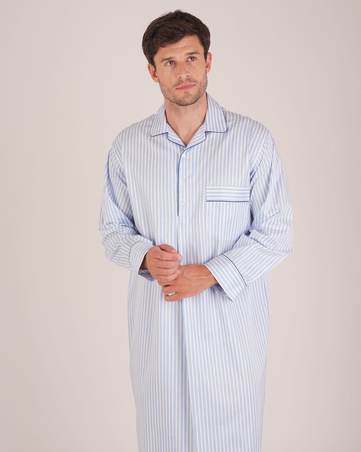 Bonsoir of London Men’s Charles Blue White Stripe Two-Fold Cotton Nightshirt, featuring a blue and white striped design, four-button placket, shirt-tail hem and generously cut fit, half body shot on a model.
