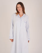 Bonsoir of London Women’s Isla Blue White Stripe Brushed Cotton Nightshirt, featuring a blue and white striped design, button placket, shirt-tail hem, piping detail, cuffs and breast pocket, half body shot on a model.