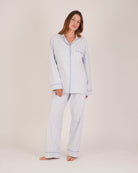 Bonsoir of London Women’s Isla Blue White Stripe Brushed Cotton Pyjamas, featuring a blue and white striped design, square-hemmed jacket, half-elasticated waist with self-fabric tie trouser, complementary piping, full body shot on a model.