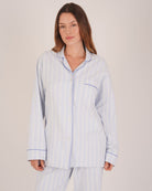 Bonsoir of London Women’s Isla Blue White Stripe Brushed Cotton Pyjamas, featuring a blue and white striped design, square-hemmed jacket, half-elasticated waist with self-fabric tie trouser, complementary piping, half body shot on a model.