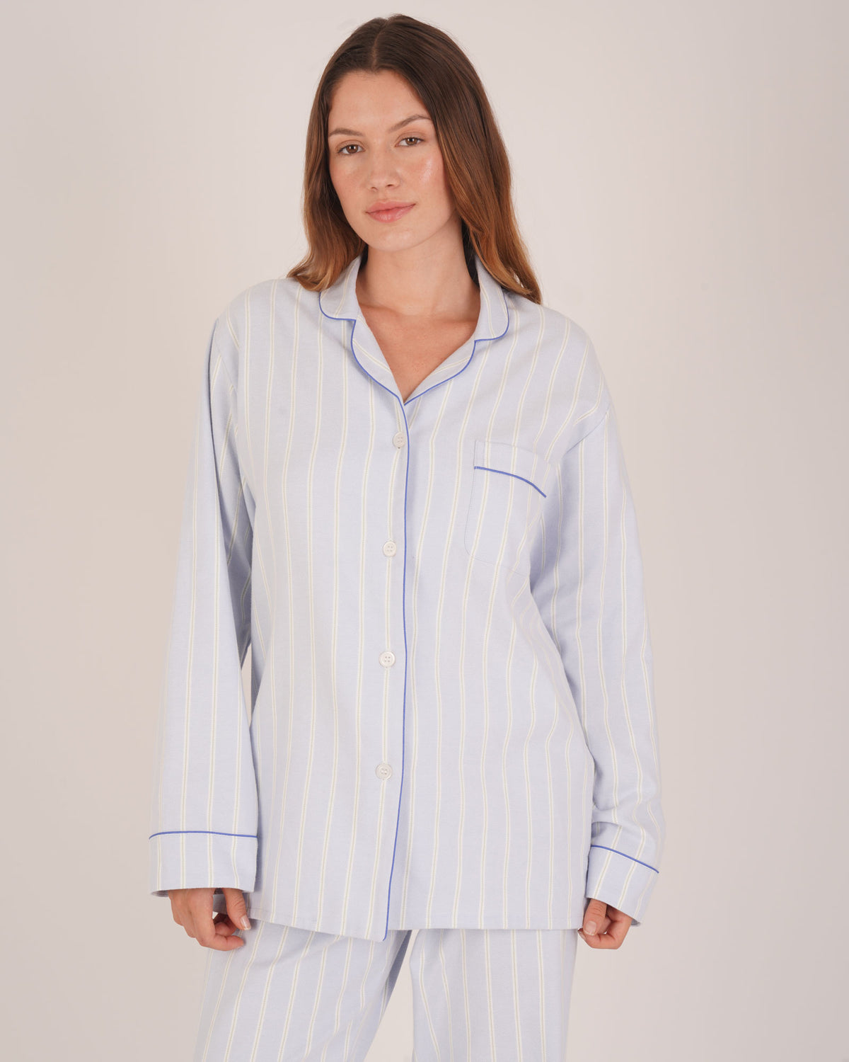 Bonsoir of London Women’s Isla Blue White Stripe Brushed Cotton Pyjamas, featuring a blue and white striped design, square-hemmed jacket, half-elasticated waist with self-fabric tie trouser, complementary piping, half body shot on a model.