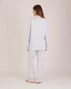 Bonsoir of London Women’s Isla Blue White Stripe Brushed Cotton Pyjamas, featuring a blue and white striped design, square-hemmed jacket, half-elasticated waist with self-fabric tie trouser, complementary piping, full body shot on a model from the back.