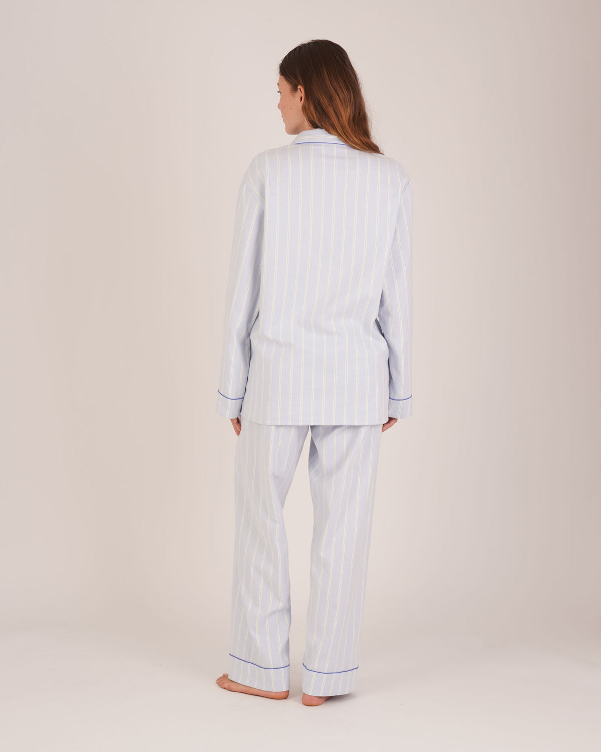 Bonsoir of London Women’s Isla Blue White Stripe Brushed Cotton Pyjamas, featuring a blue and white striped design, square-hemmed jacket, half-elasticated waist with self-fabric tie trouser, complementary piping, full body shot on a model from the back.