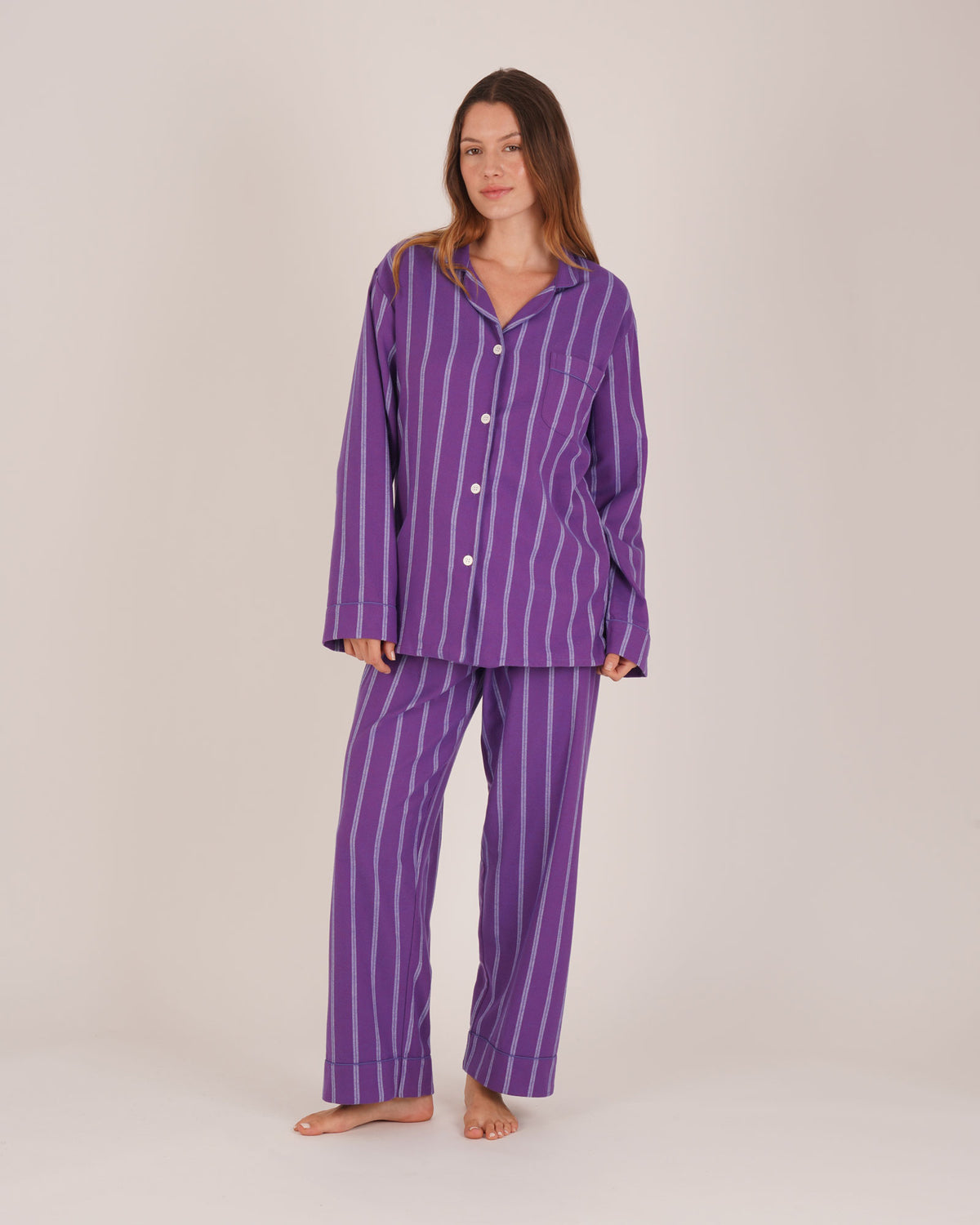 Bonsoir of London Women’s Lily Purple Stripe Brushed Cotton Pyjamas, featuring a purple striped design, square-hemmed jacket, half-elasticated waist with self-fabric tie trouser, complementary piping, full body shot on a model.