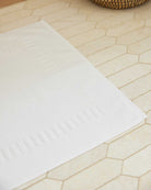Bonsoir of London 100% Cotton Bathmat in white, detail close-up on a tile floor.