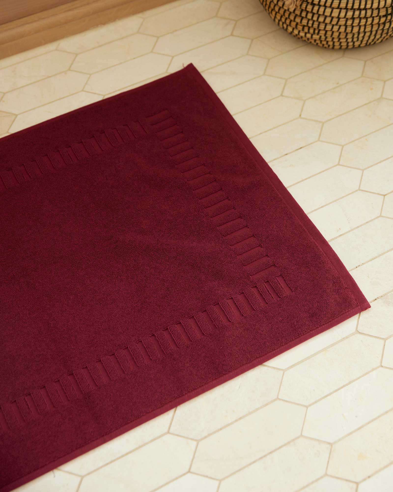 Bonsoir of London 100% Cotton Bathmat in burgundy, detail close-up on a tile floor.