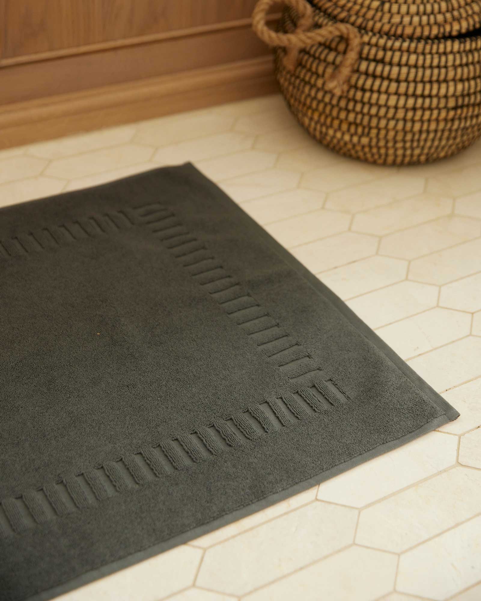 Bonsoir of London 100% Cotton Bathmat in charcoal grey, detail close-up on a beige tile floor.