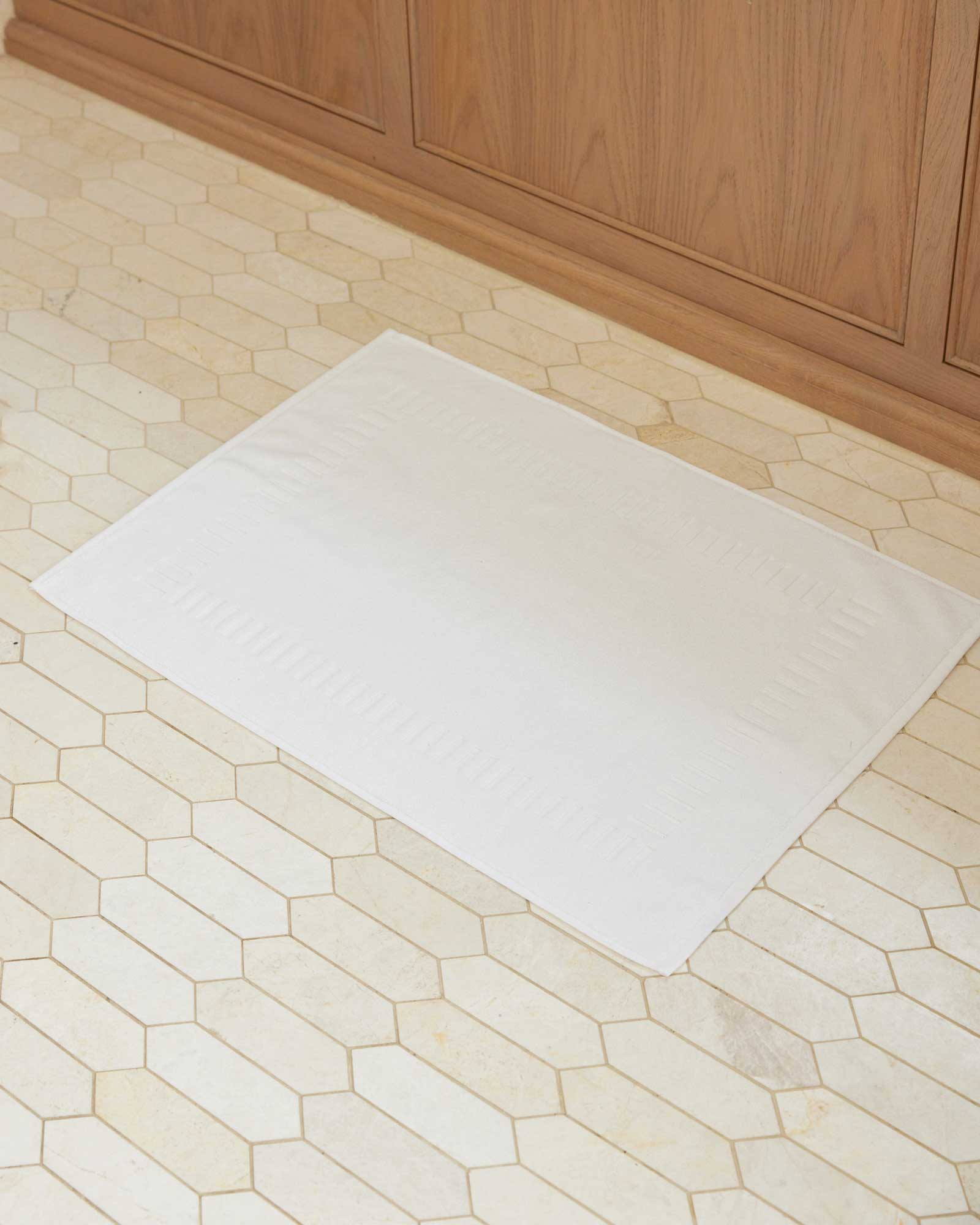Bonsoir of London 100% Cotton Bathmat in white, lifestyle shot on a tile floor.