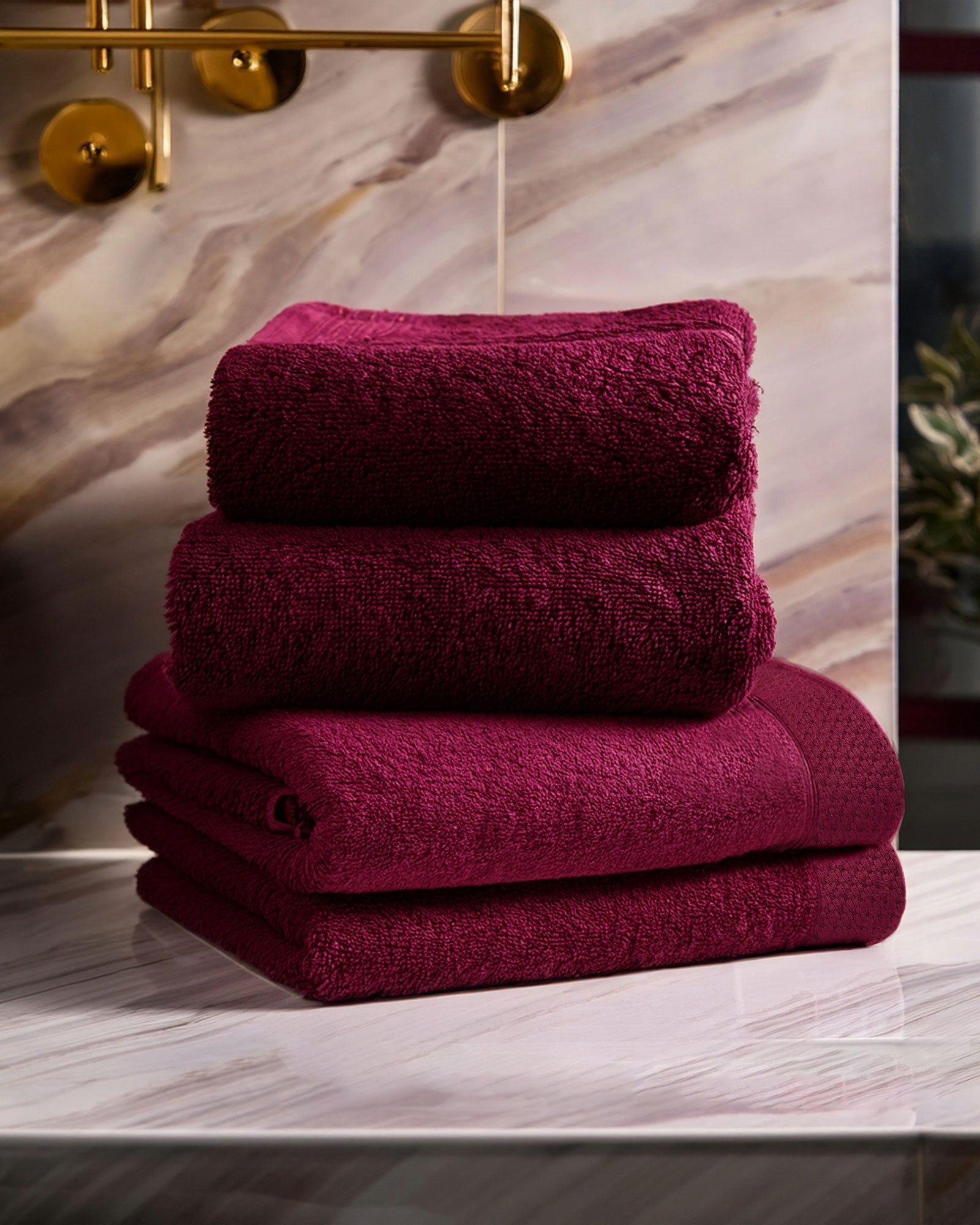 Stack of burgundy towels on a marble surface with a gold light fixture in the background.
