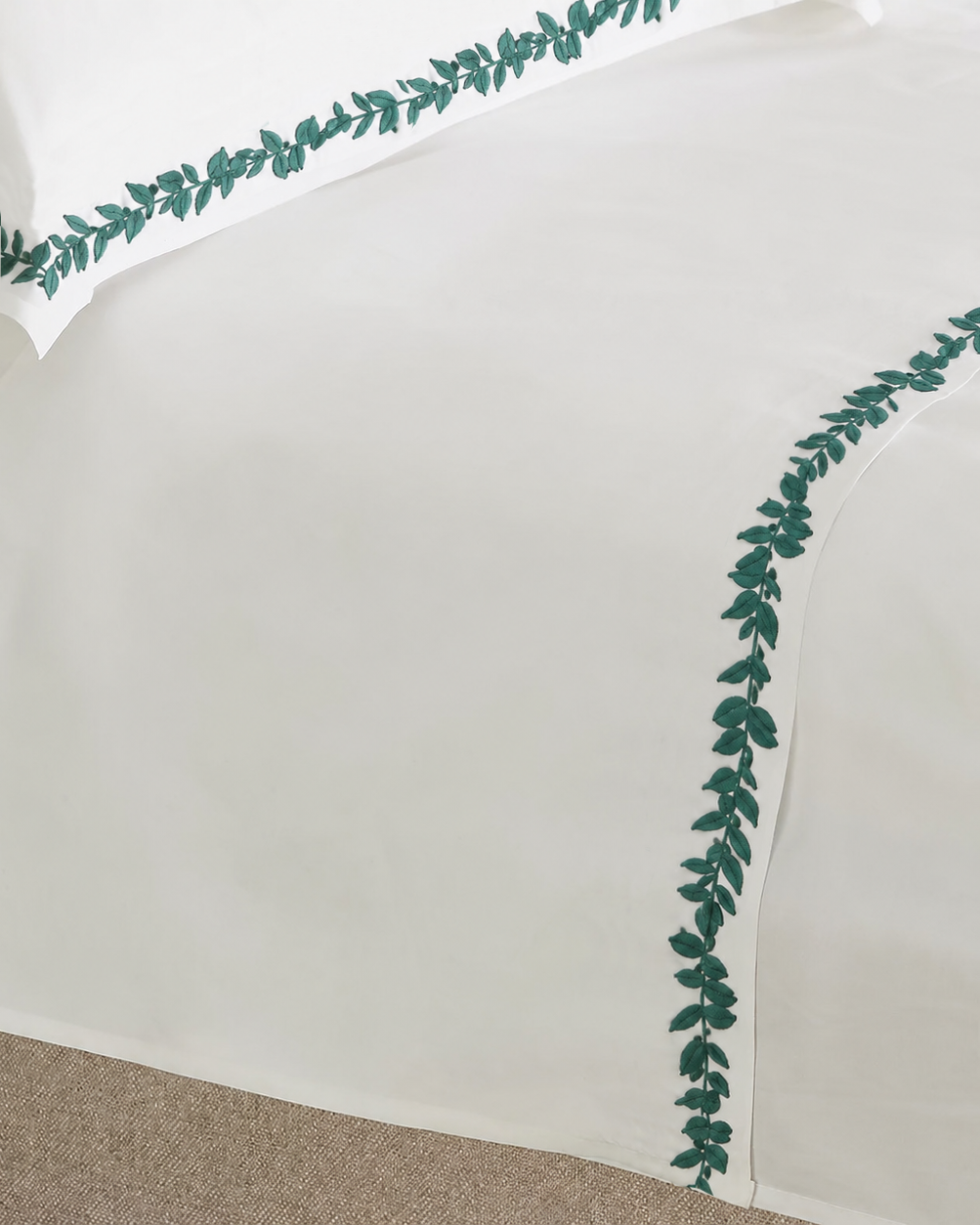 Bonsoir of London White flat sheet with green leaf border on a beige bed.