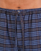 Bonsoir of London Men’s Theodore Blue Plaid Brushed Cotton Pyjama Trousers, featuring a blue and navy plaid design, 100% brushed cotton, fully elasticated waist, concealed button fly, self-fabric drawstring tie and pockets, close up shot on a model.