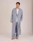 Bonsoir of London Men’s Arthur Blue Check Brushed Cotton Dressing Gown, featuring a soft blue, white and navy check design, shawl collar, wide tie belt, patch pockets, full body shot on a model.