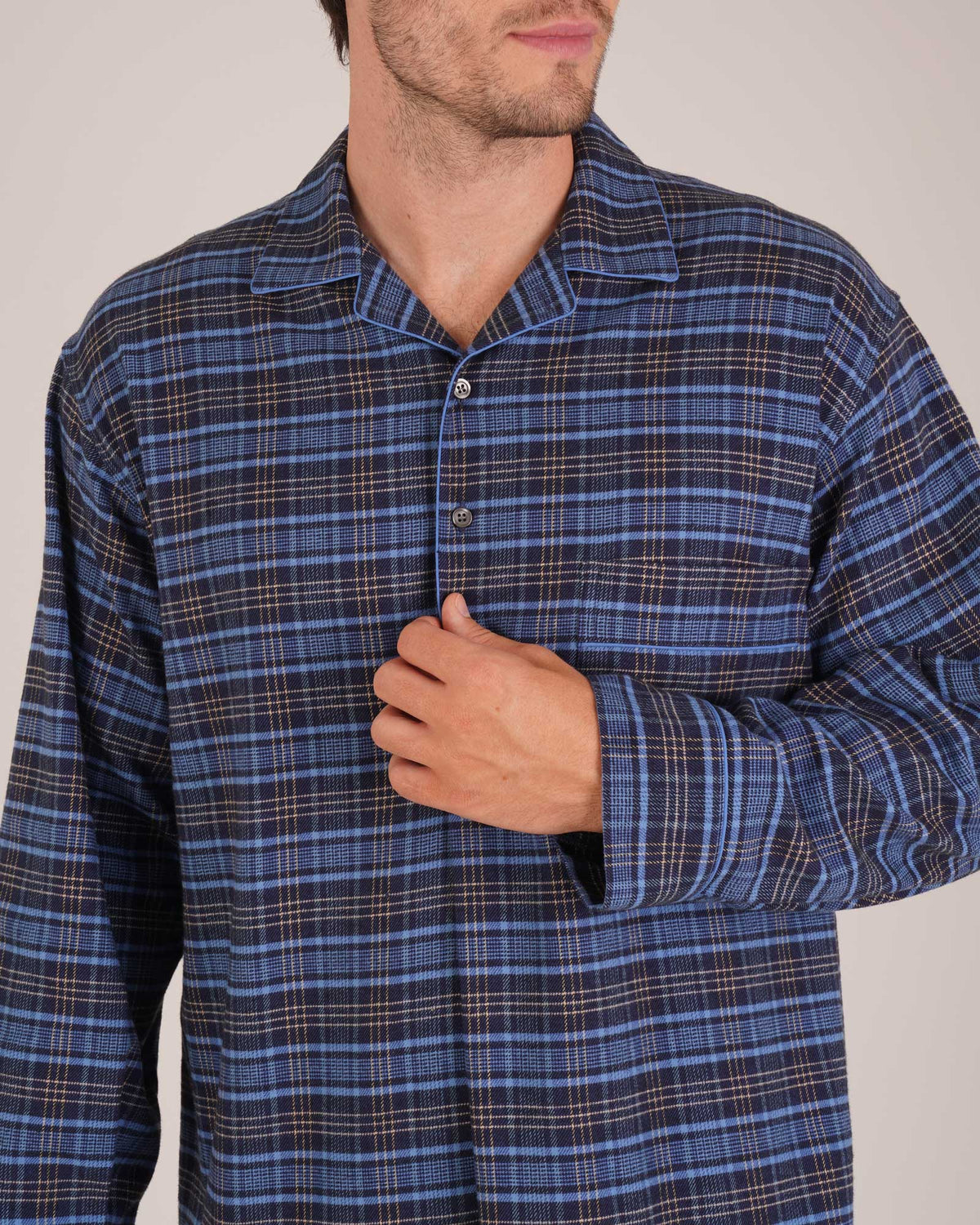 Bonsoir of London Men’s Theodore Blue Plaid Brushed Cotton Nightshirt, featuring a blue and navy plaid design with subtle gold detailing, four-button placket, shirt-tail hem and generously cut fit, close up shot on a model.