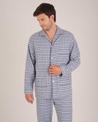 Bonsoir of London Men’s Arthur Blue Check Brushed Cotton Pyjamas, featuring a blue, pale blue, white and navy check design, three jacket pockets, elasticated-waist trousers, button fastening and concealed button fly, half body shot on a model.