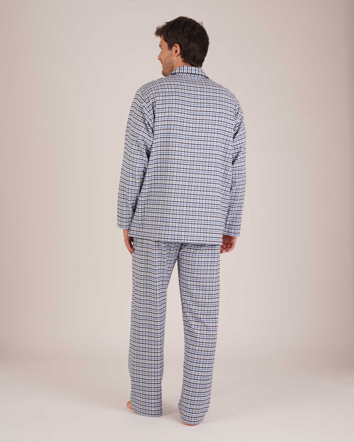 Bonsoir of London Men’s Arthur Blue Check Brushed Cotton Pyjamas, featuring a blue, pale blue, white and navy check design, three jacket pockets, elasticated-waist trousers, button fastening and concealed button fly, full body shot on a model from the back.