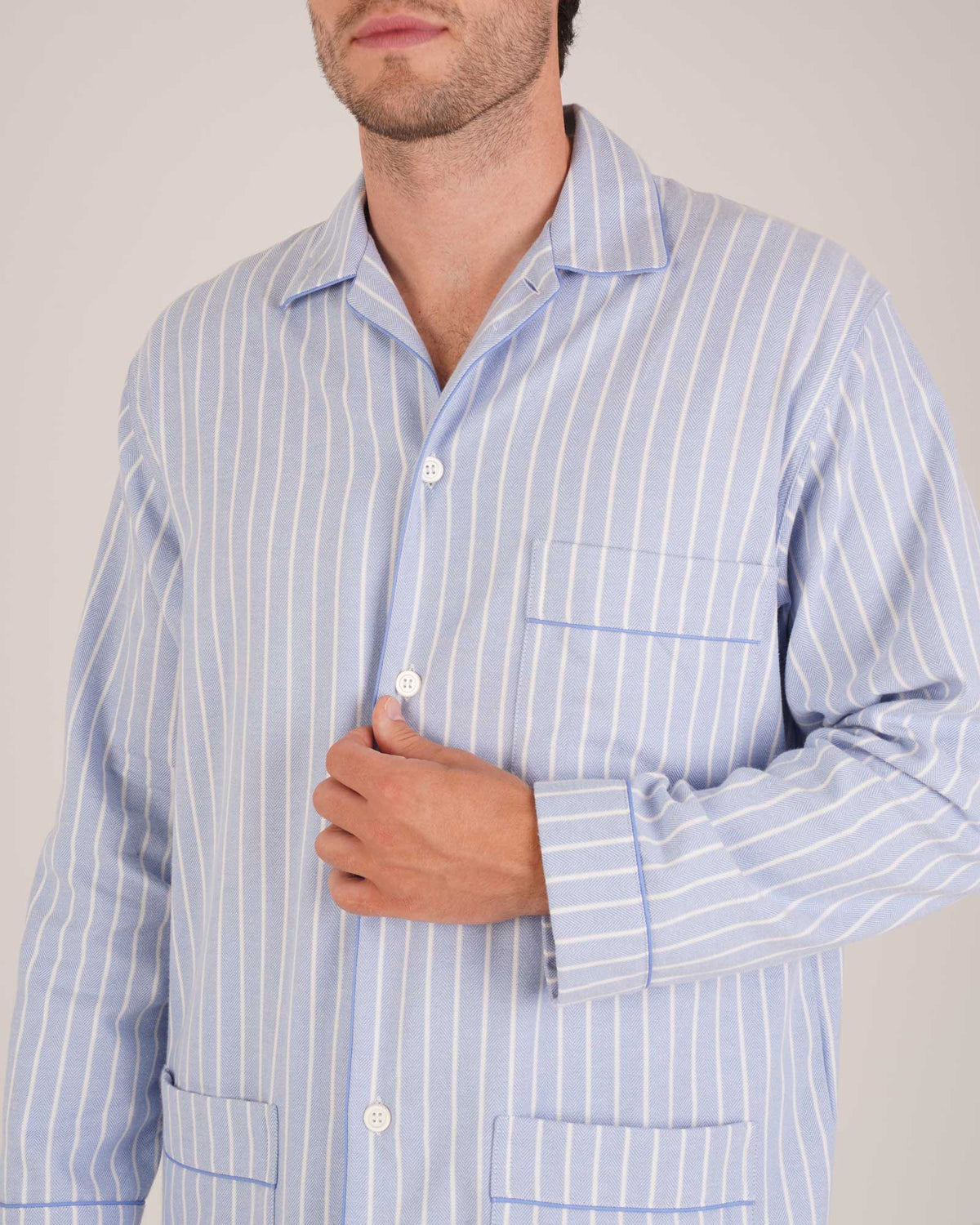 Bonsoir of London Men’s Oliver Blue White Stripe Brushed Cotton Pyjamas, featuring a pale blue and white striped design, three jacket pockets, elasticated-waist trousers, button fastening and concealed button fly, close up shot on a model.