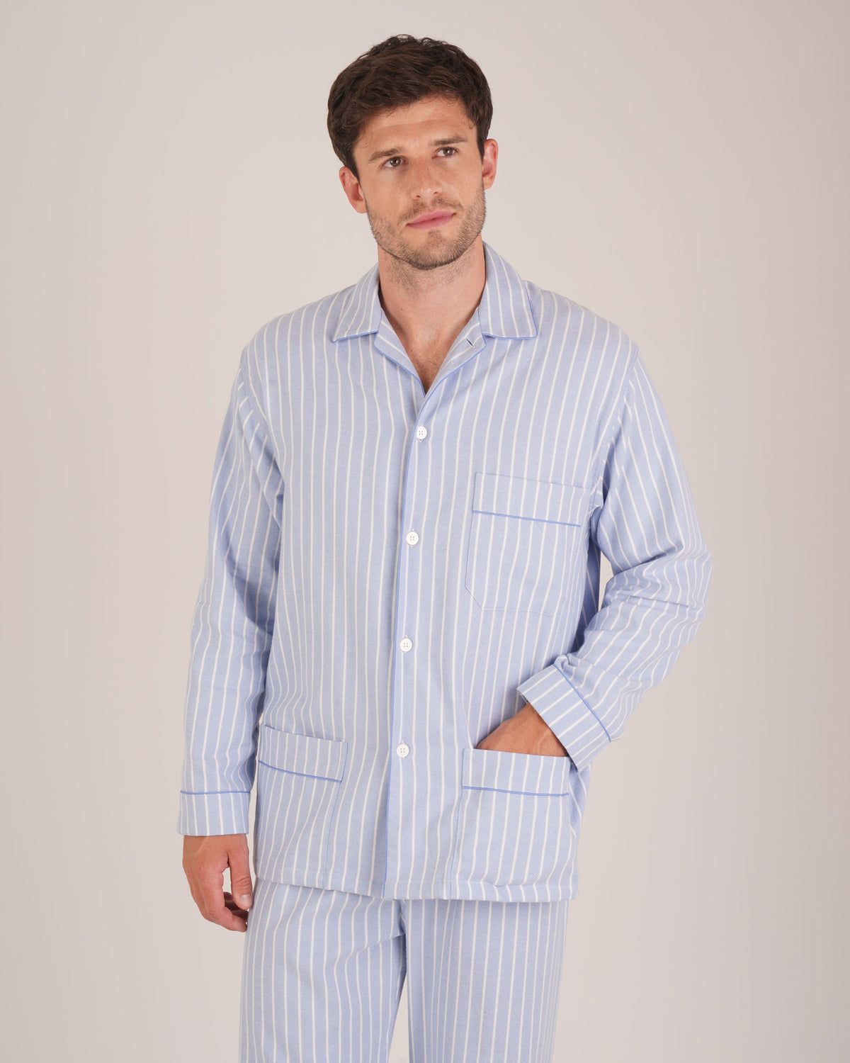 Bonsoir of London Men’s Oliver Blue White Stripe Brushed Cotton Pyjamas, featuring a pale blue and white striped design, three jacket pockets, elasticated-waist trousers, button fastening and concealed button fly, half body shot on a model.