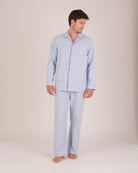 Bonsoir of London Men’s Oliver Blue White Stripe Brushed Cotton Pyjamas, featuring a pale blue and white striped design, three jacket pockets, elasticated-waist trousers, button fastening and concealed button fly, full body shot on a model.
