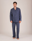 Bonsoir of London Men’s Theodore Blue Plaid Brushed Cotton Pyjamas, featuring a blue and navy plaid design with subtle gold detailing, three jacket pockets, elasticated-waist trousers, button fastening and concealed button fly, full body shot on a model.
