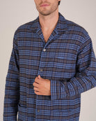 Bonsoir of London Men’s Theodore Blue Plaid Brushed Cotton Pyjamas, featuring a blue and navy plaid design with subtle gold detailing, three jacket pockets, elasticated-waist trousers, button fastening and concealed button fly, close up shot on a model.