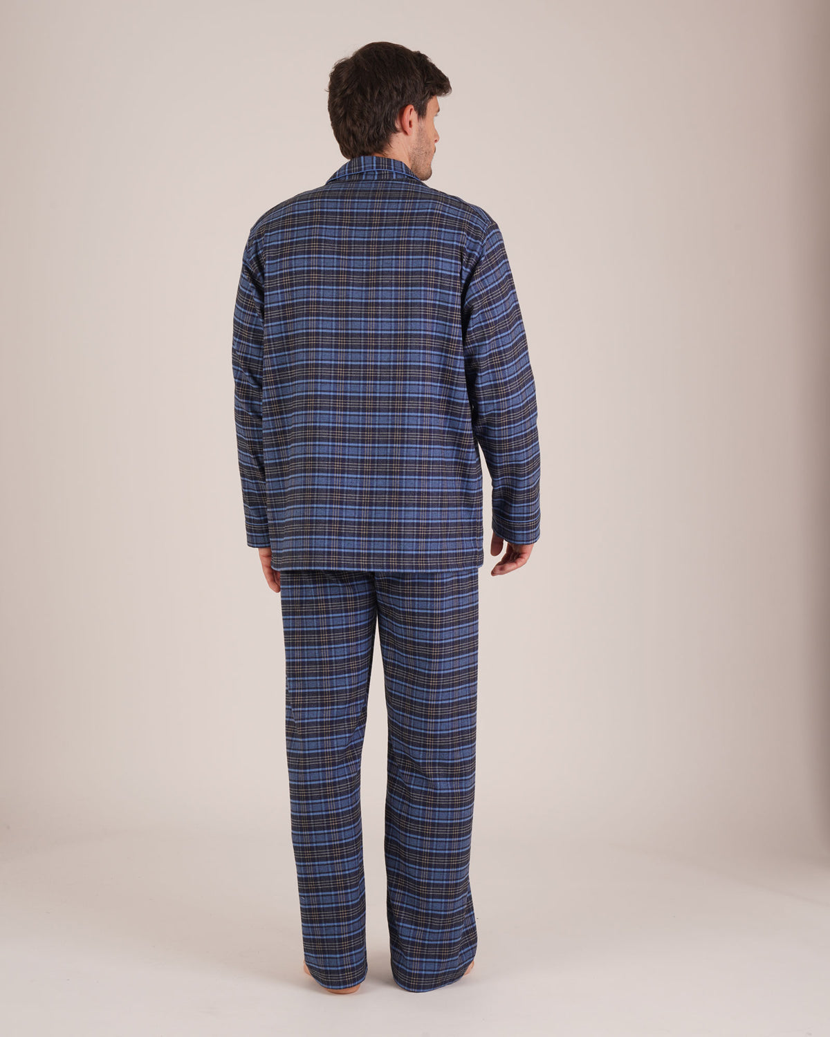 Bonsoir of London Men’s Theodore Blue Plaid Brushed Cotton Pyjamas, featuring a blue and navy plaid design with subtle gold detailing, three jacket pockets, elasticated-waist trousers, button fastening and concealed button fly, full body shot on a model from the back.
