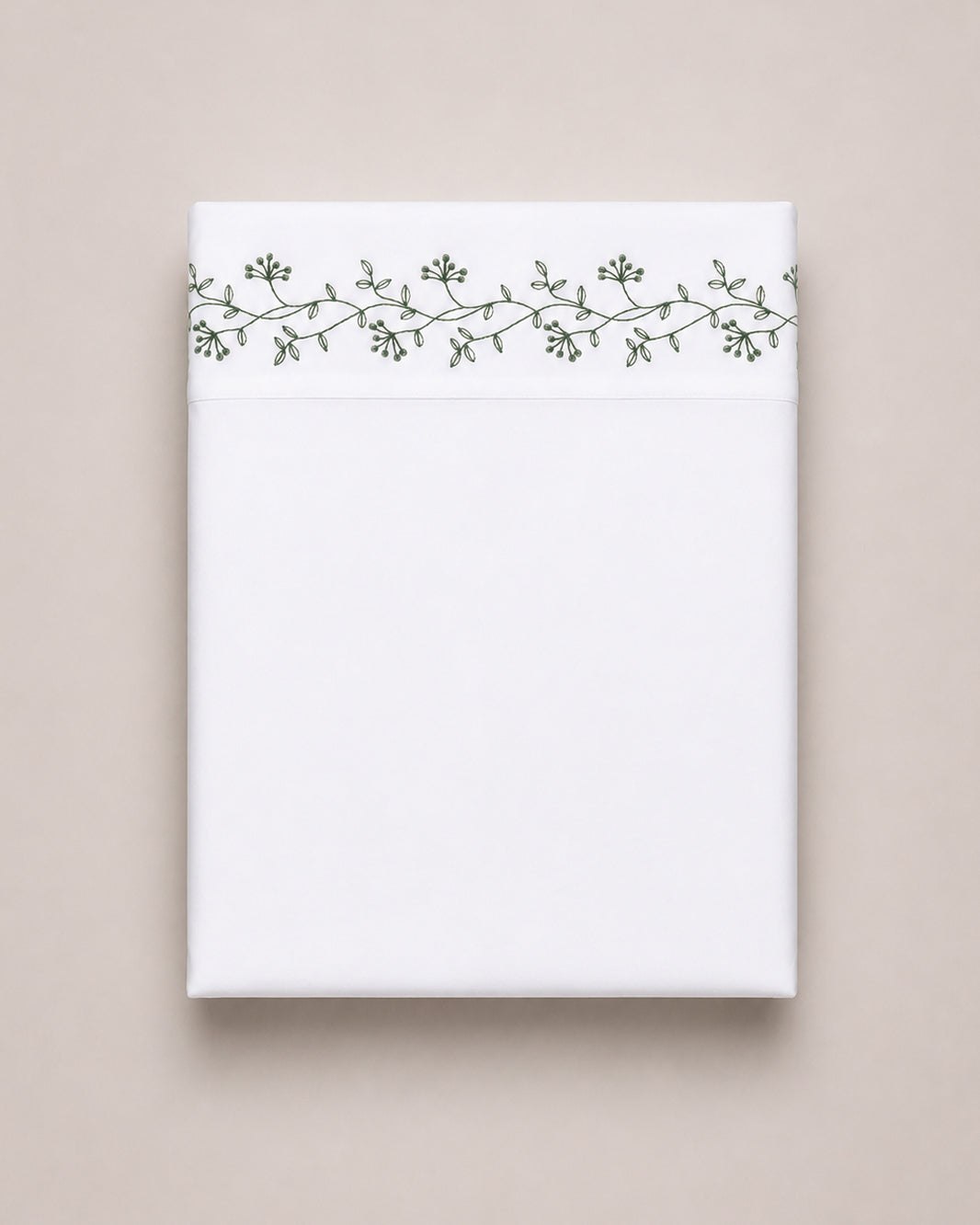 Bonsoir of London cotton white flat sheet with green floral embroidery, folded on a beige studio background.