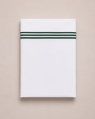 Bonsoir of London white cotton flat sheets with three green embroidered stripes, folded on a studio background.