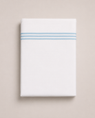 Bonsoir of London white cotton flat sheets with 3 light blue embroidered stripes, folded on a studio background.