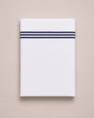 Bonsoir of London white cotton flat sheets with three navy embroidered stripes, folded on a studio background.