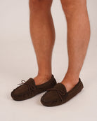 Bonsoir of London Men’s Othello Sheepskin Slippers in Brown, featuring soft suede with natural sheepskin lining, traditional hand-stitched detailing, leather lace trim and rubber sole, product shot on model.