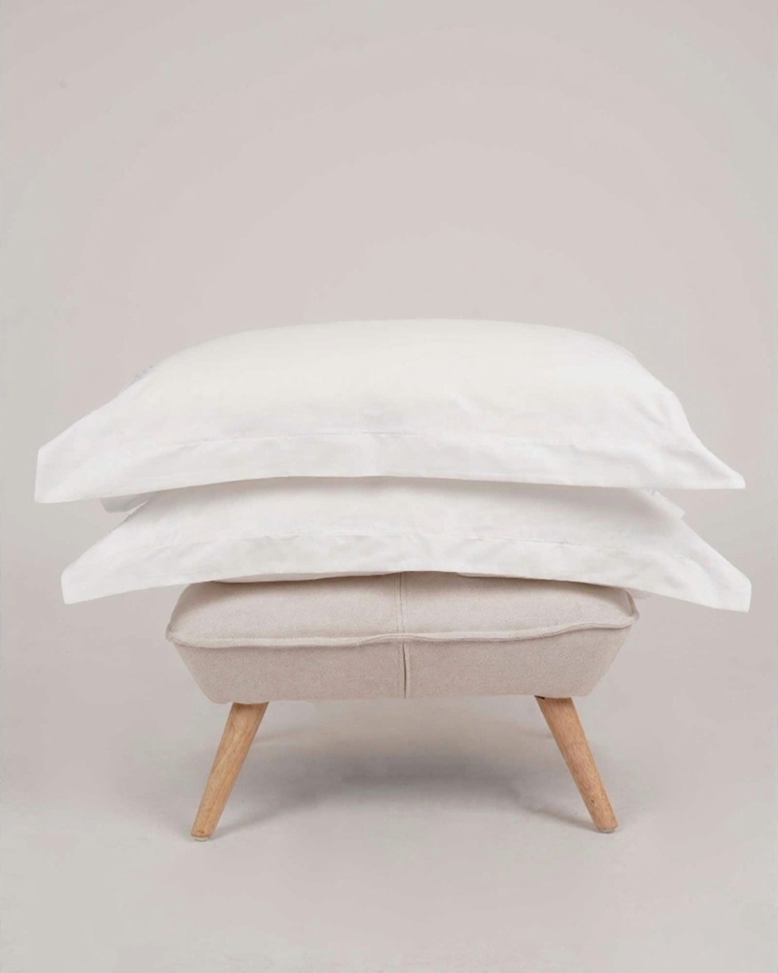 Bonsoir of London 100% Cotton Oxford Pillowcases White, set of 2 on a fabric stool shot in a studio.